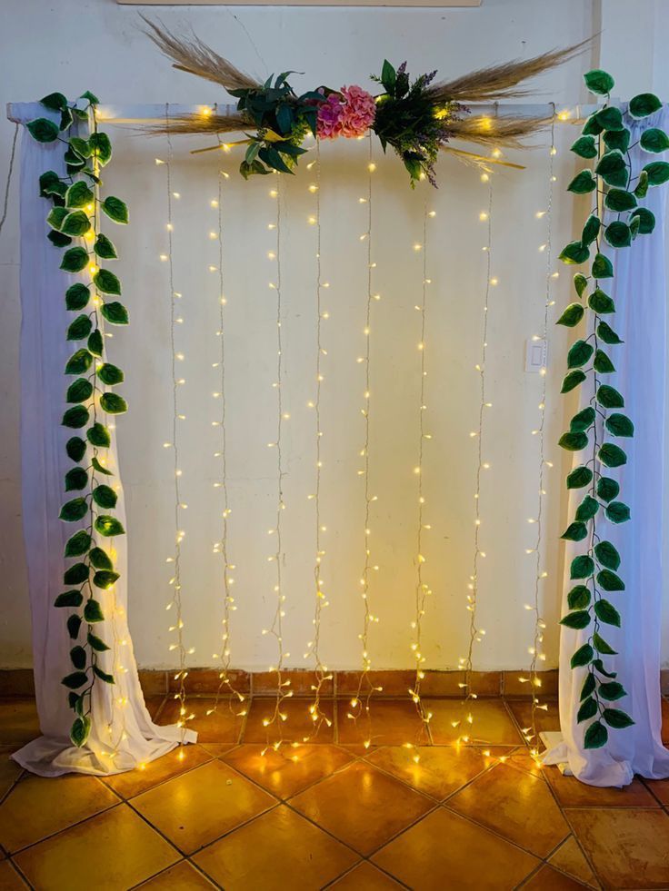 a white backdrop with lights and greenery on the side, along with curtains that are draped over it