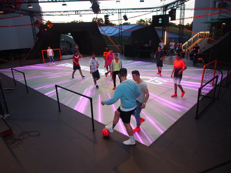 a group of men playing soccer on an indoor field with lights and people watching from the sidelines