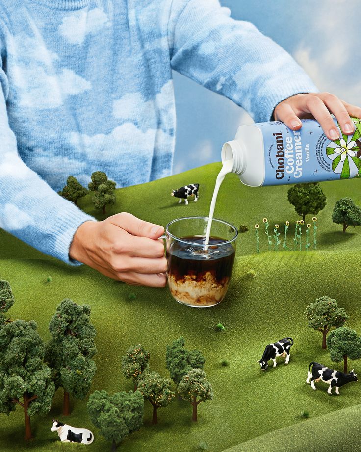 a person pouring something into a cup with cows on the ground in front of them