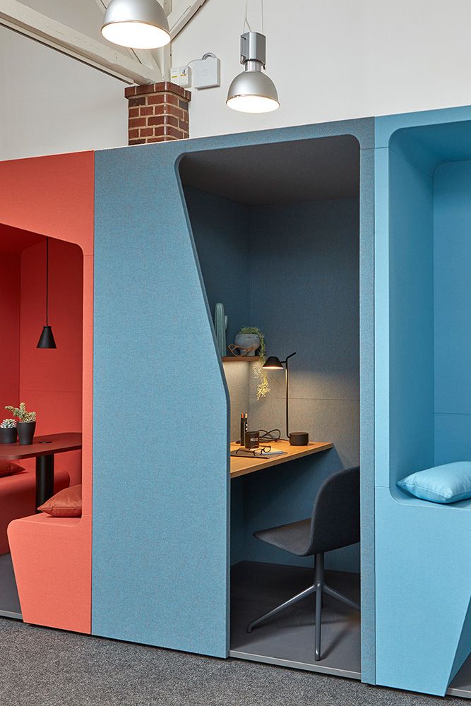 an office cubicle with blue and red walls, two chairs and a desk in the corner