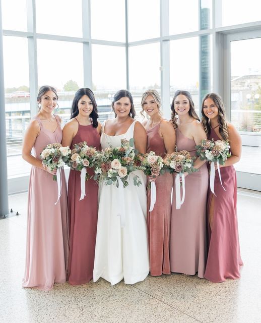 a group of women standing next to each other in front of a window holding bouquets