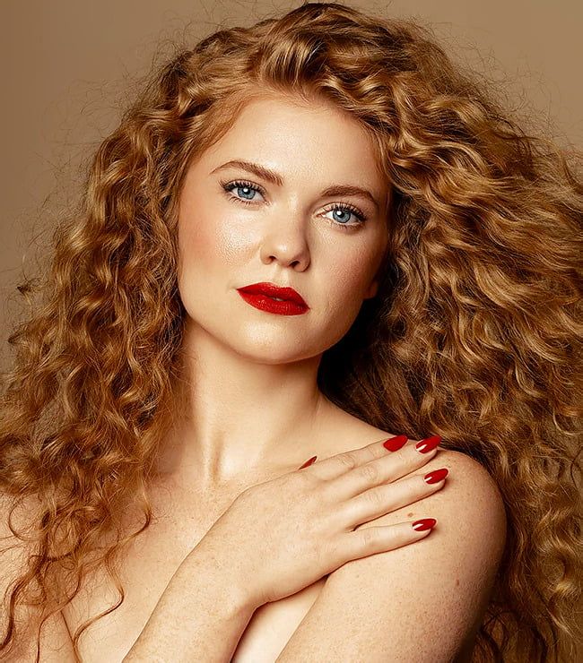 a woman with long red hair and bright blue eyes is posing for the camera, her hands on her chest