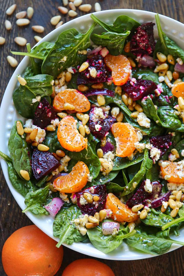 a salad with spinach, oranges and nuts in a white bowl on a wooden table