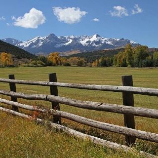 a wooden fence in the middle of a grassy field with mountains in the back ground