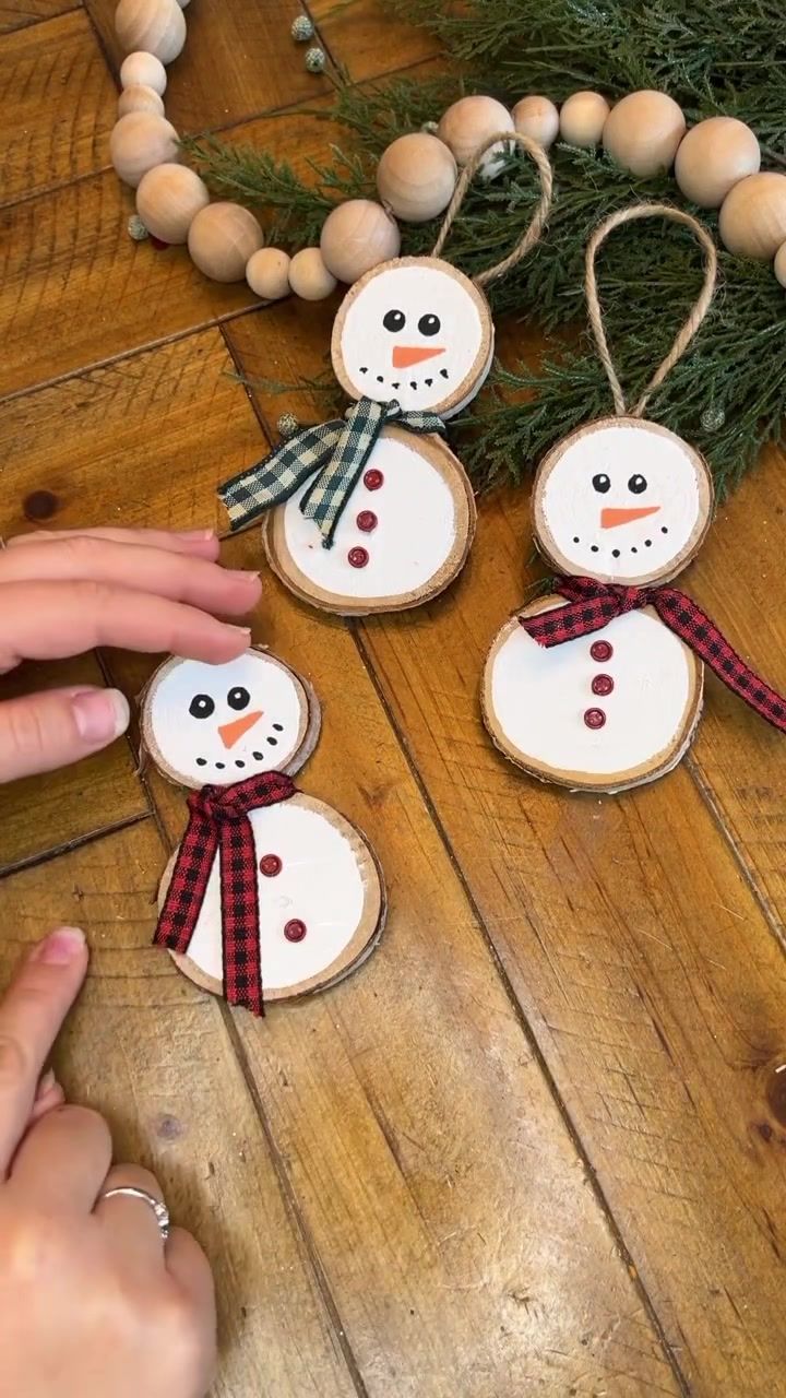 three snowmen made out of wood slices on a wooden table next to a christmas tree