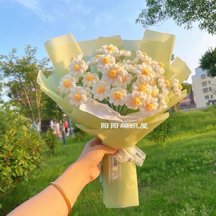 a hand holding a bouquet of white and yellow flowers in front of a grassy area