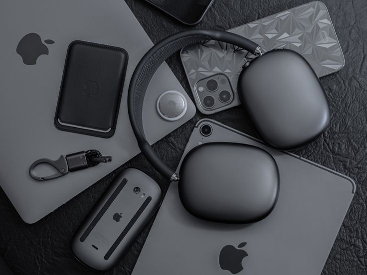 an apple computer and other electronic devices on a black leather surface with mouse, keyboard, headphones, charger, card reader and more