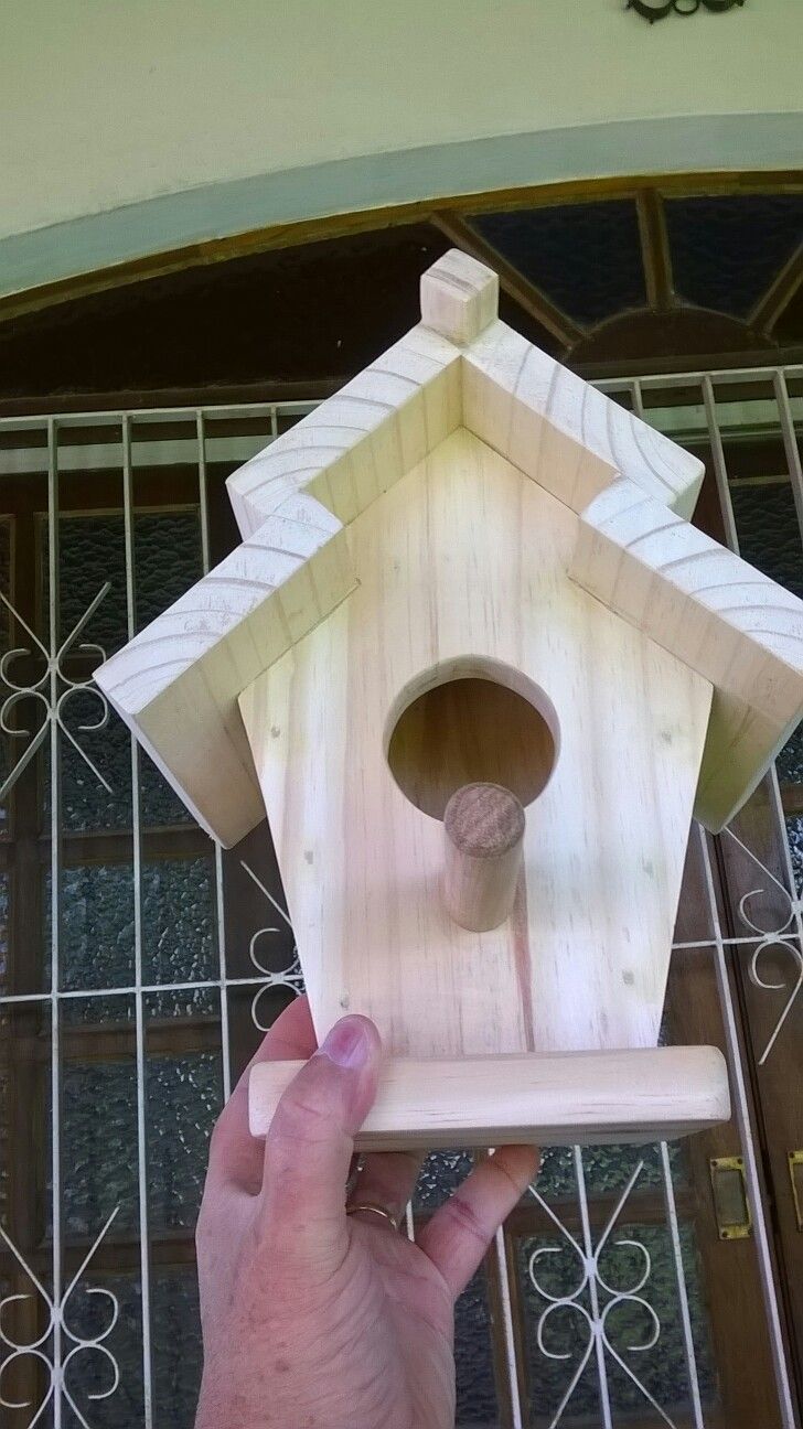 a hand holding a wooden birdhouse in front of a metal door with an arched window