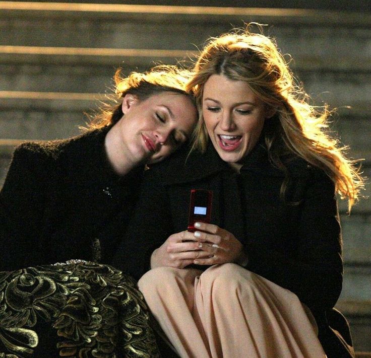 two women sitting on the steps looking at a cell phone and laughing with each other