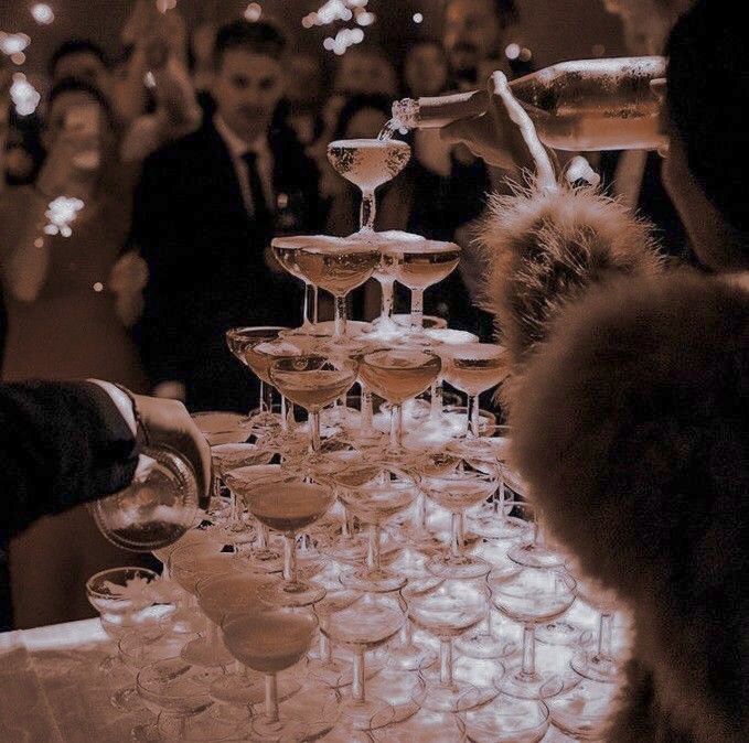 a table topped with lots of wine glasses filled with different types of drinks and people in the background