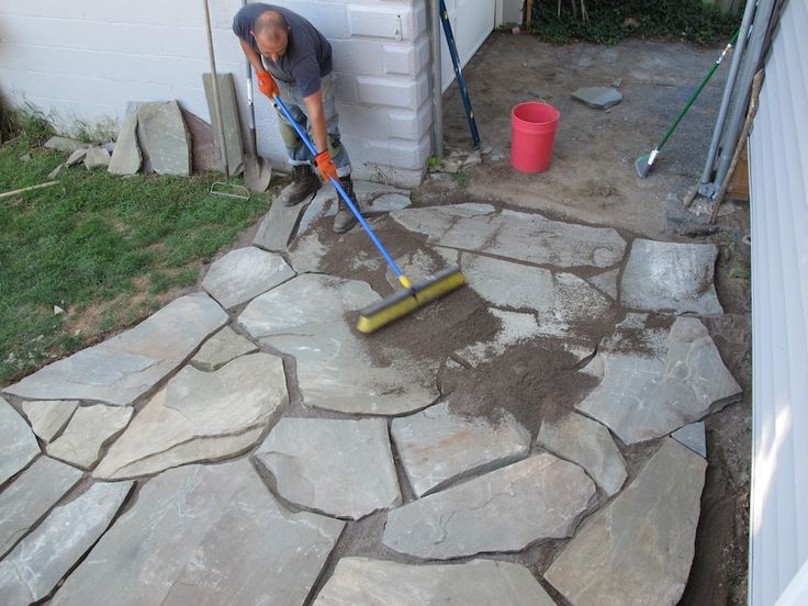 a man with a mop and bucket digging in the dirt on top of a stone walkway