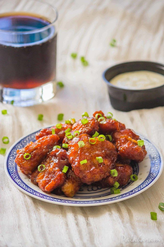 chicken wings with sauce and green onions on a plate next to a glass of tea