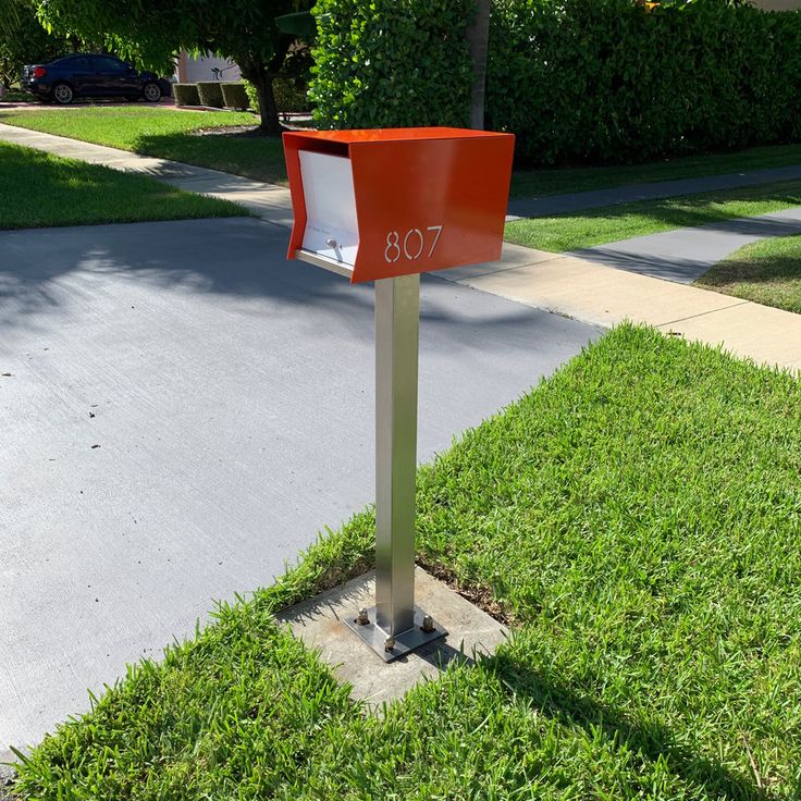 an orange mailbox sitting on the side of a road next to a tree and grass covered sidewalk