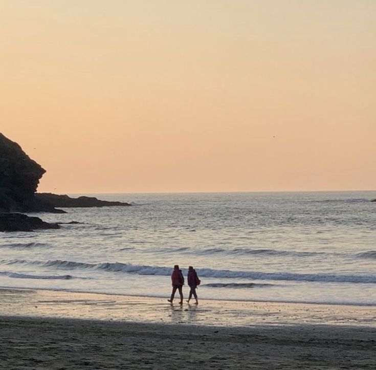 two people walking on the beach at sunset with an ocean view in the back ground