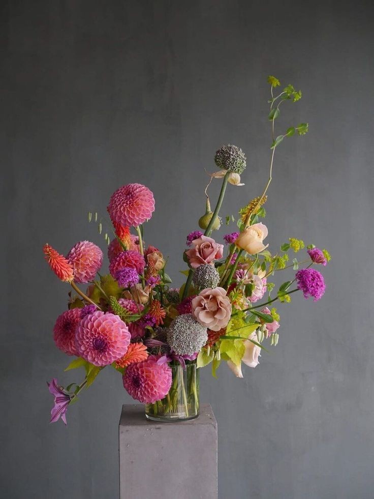 a vase filled with lots of colorful flowers on top of a wooden table next to a gray wall