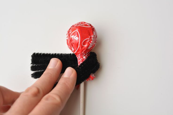 a hand holding a red and black heart shaped lollipop on a white surface