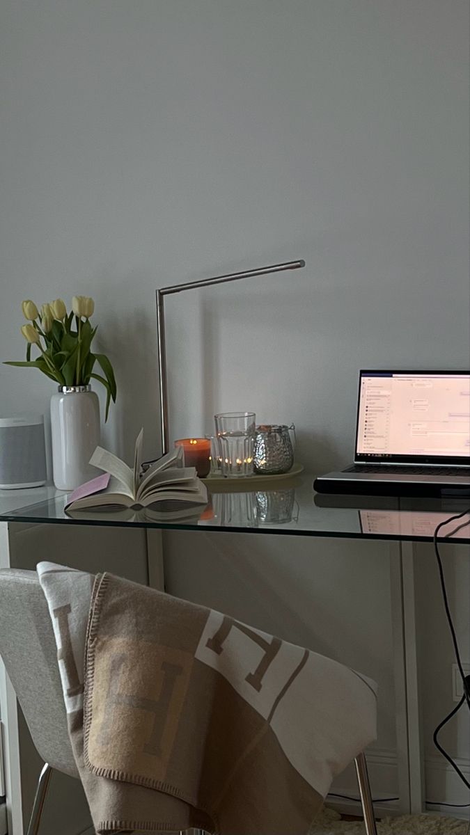 a laptop computer sitting on top of a glass desk next to a vase with flowers