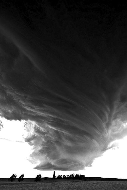 a black and white photo of clouds in the sky over a grassy field with trees