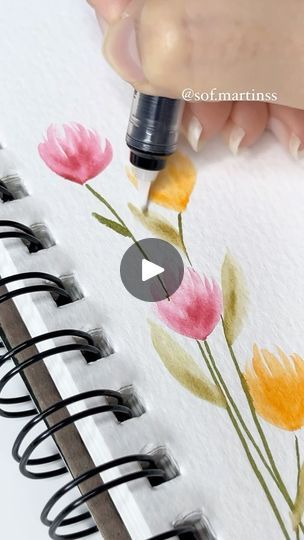 someone is drawing flowers on the paper with a pen and inking them into watercolors