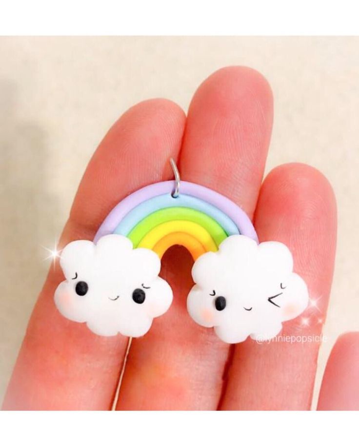 a hand holding two tiny clouds with a rainbow in the middle