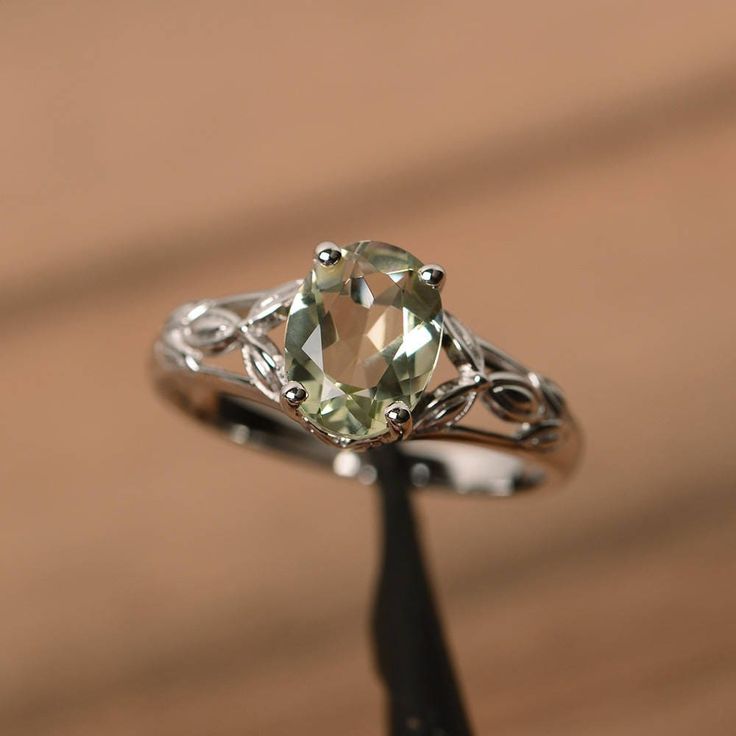 a fancy ring with an oval cut green stone in the center, on a piece of wood