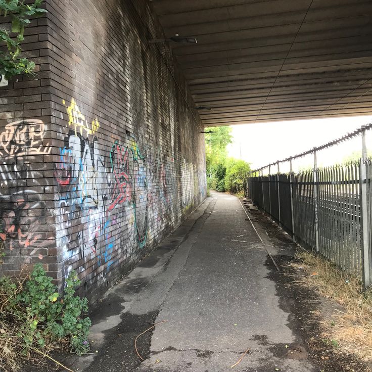 graffiti on the side of a brick wall under an overpass near a fenced in area