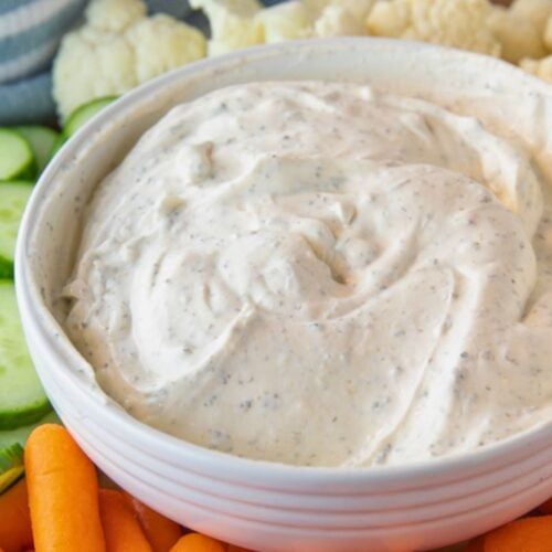 a white bowl filled with dip surrounded by carrots and cauliflower