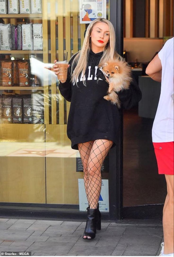 a woman in fishnet stockings is holding a small dog while walking down the street