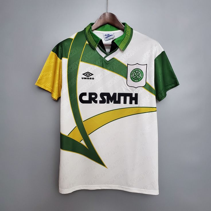 a green and white soccer jersey hanging on a hanger in front of a gray wall