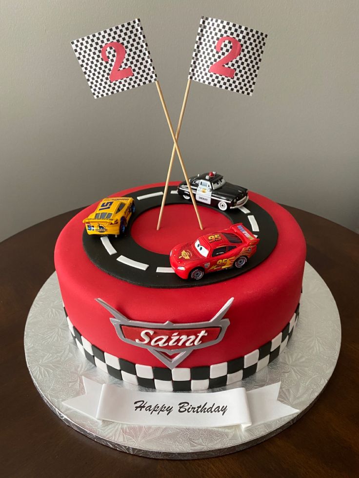 a birthday cake with cars on it and two flags sticking out of the top one