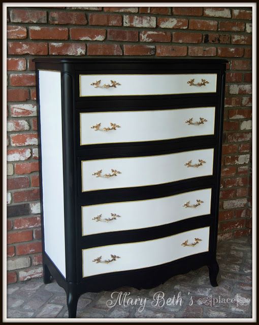 a black and white dresser with gold hardware on the bottom drawer, against a brick wall