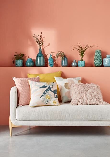 a couch with pillows and vases on top of it in front of a pink wall