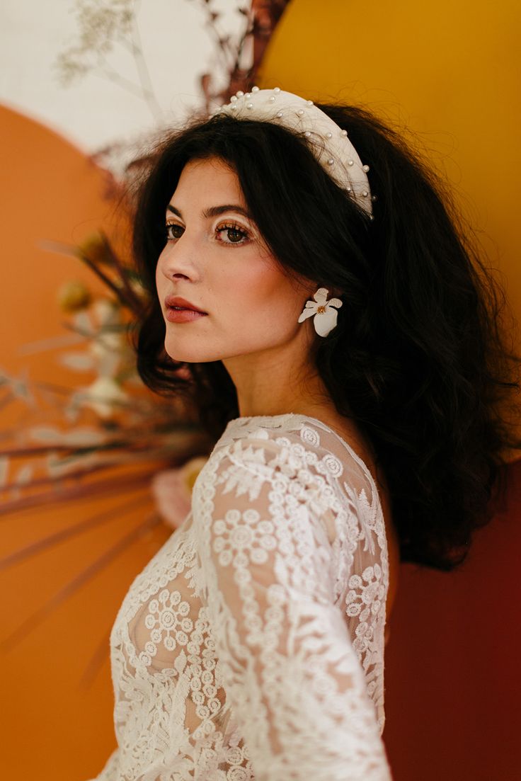 a woman wearing a white dress and holding an umbrella in front of a wall with flowers on it