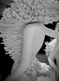 a black and white photo of a woman in a dress made out of paper sticks