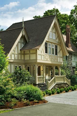 a white house with brown shingles on the roof and windows, surrounded by greenery