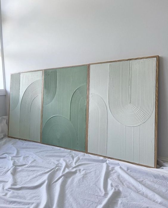 three paneled artwork displayed on a bed in a room with white sheets and pillows