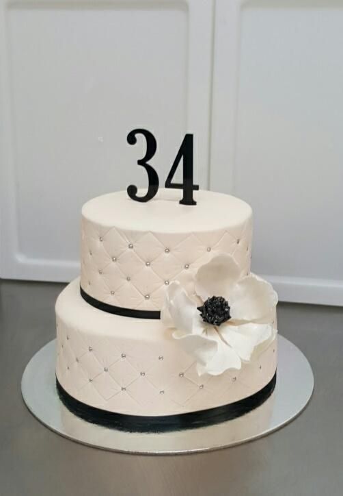 a three tiered cake with white flowers and black ribbon on the top is displayed in front of a door