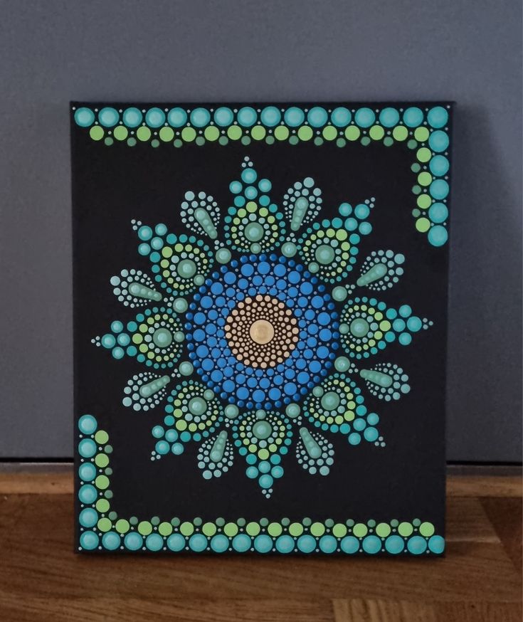 a blue and green painting on a wooden table next to a black wall with polka dots