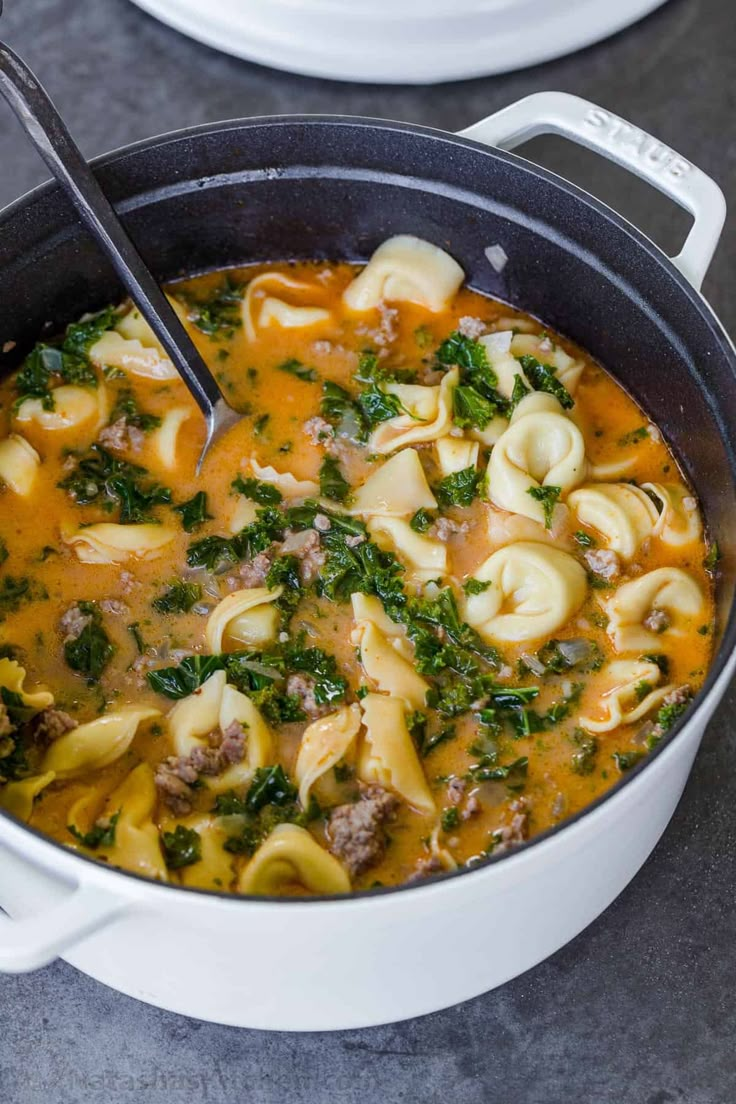 a pot filled with pasta and spinach soup on top of a gray countertop