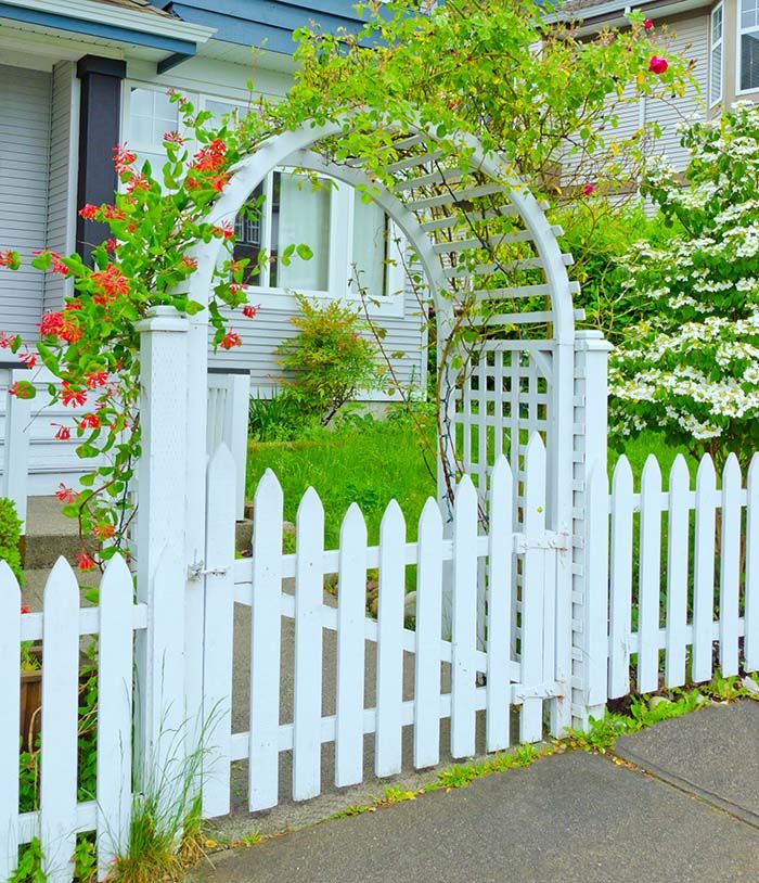 a white picket fence in front of a house with flowers growing on the top and bottom