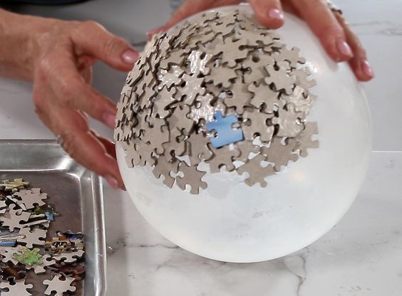 a person is holding a puzzle ball over a pan filled with pieces that have been put together