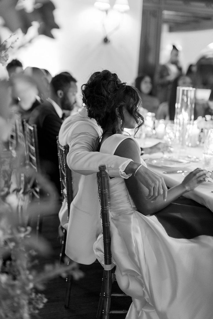 the bride and groom are sitting at the dinner table with their hands on each other's shoulders