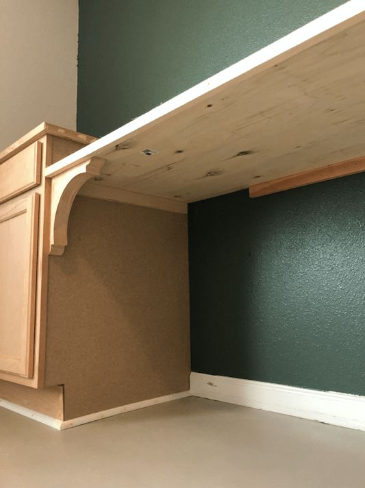 an empty room with green walls and wooden cabinets in the corner, under a shelf