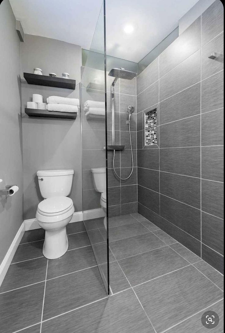 a bathroom with gray tiles and white fixtures, including a toilet and walk in shower