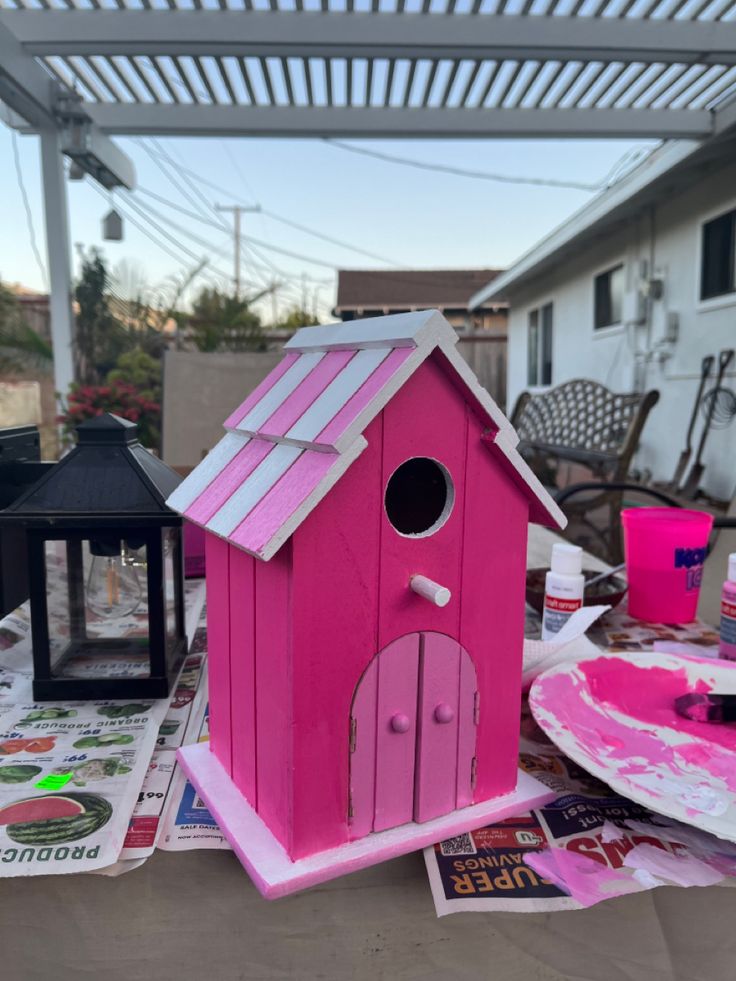 a pink birdhouse sitting on top of a table next to a plate and cup