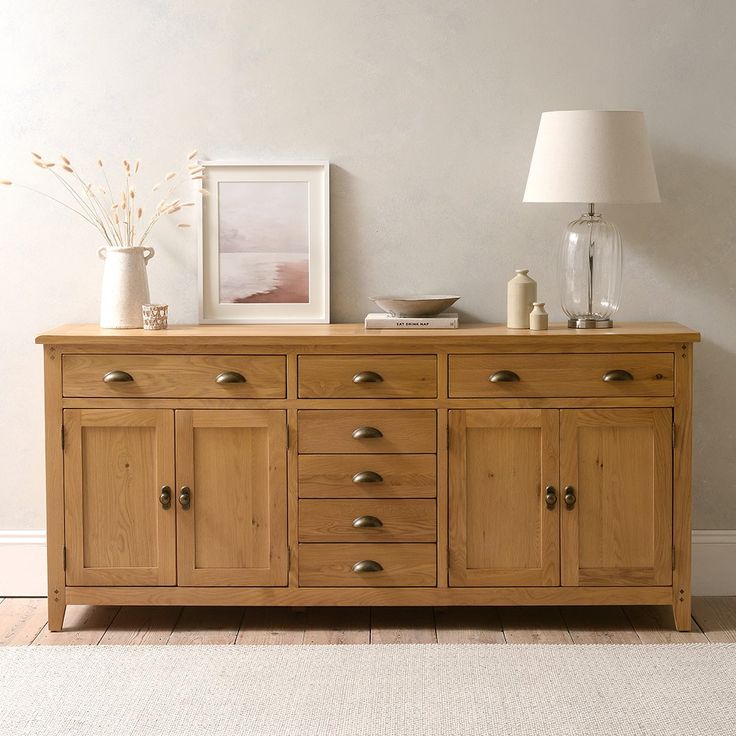 a wooden dresser with two lamps on top of it next to a white rug and wall