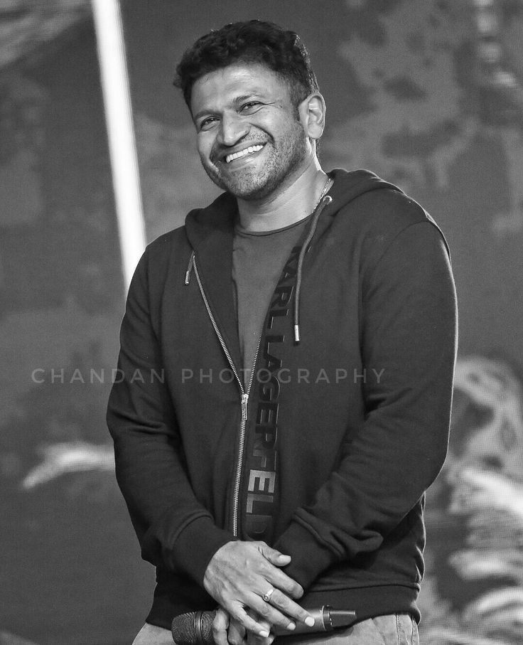 a black and white photo of a smiling man in front of a wall with graffiti