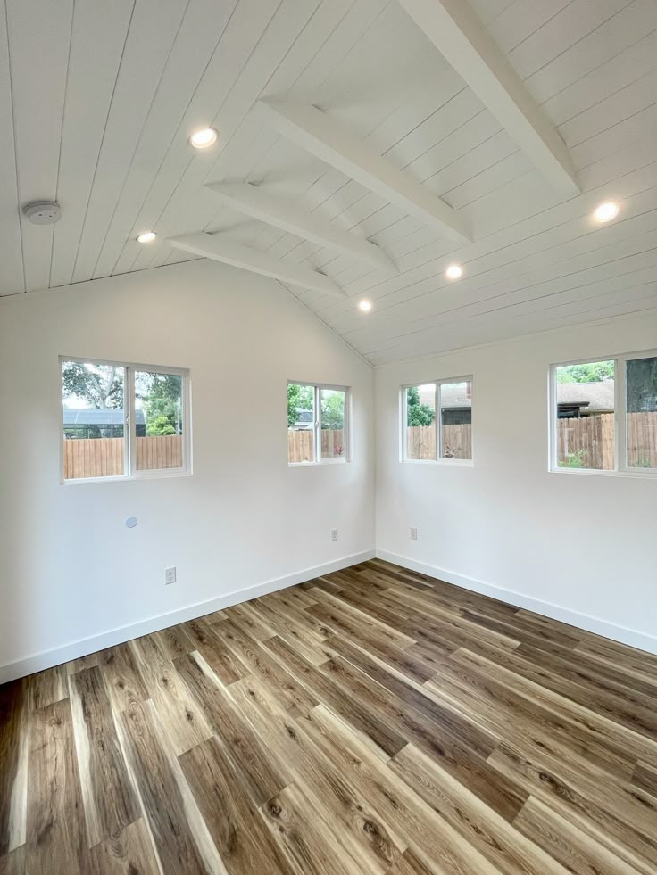 an empty room with white walls and wood flooring in the foreground, three windows on each side