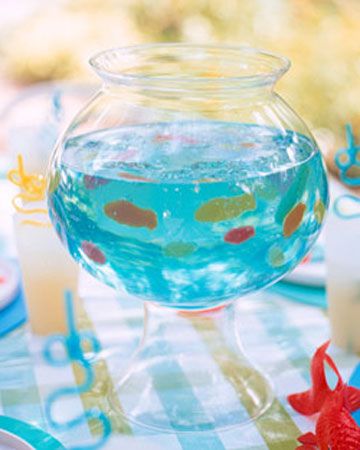 a fish bowl filled with blue liquid on top of a table covered in plates and napkins