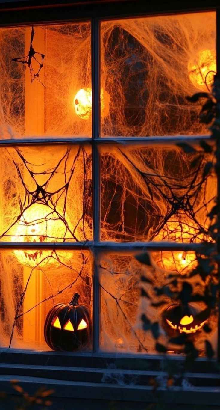 halloween pumpkins are lit up in the window at night, with spider webs on them